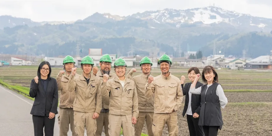 山あいの田畑を背景に笑顔で並ぶ社員たち