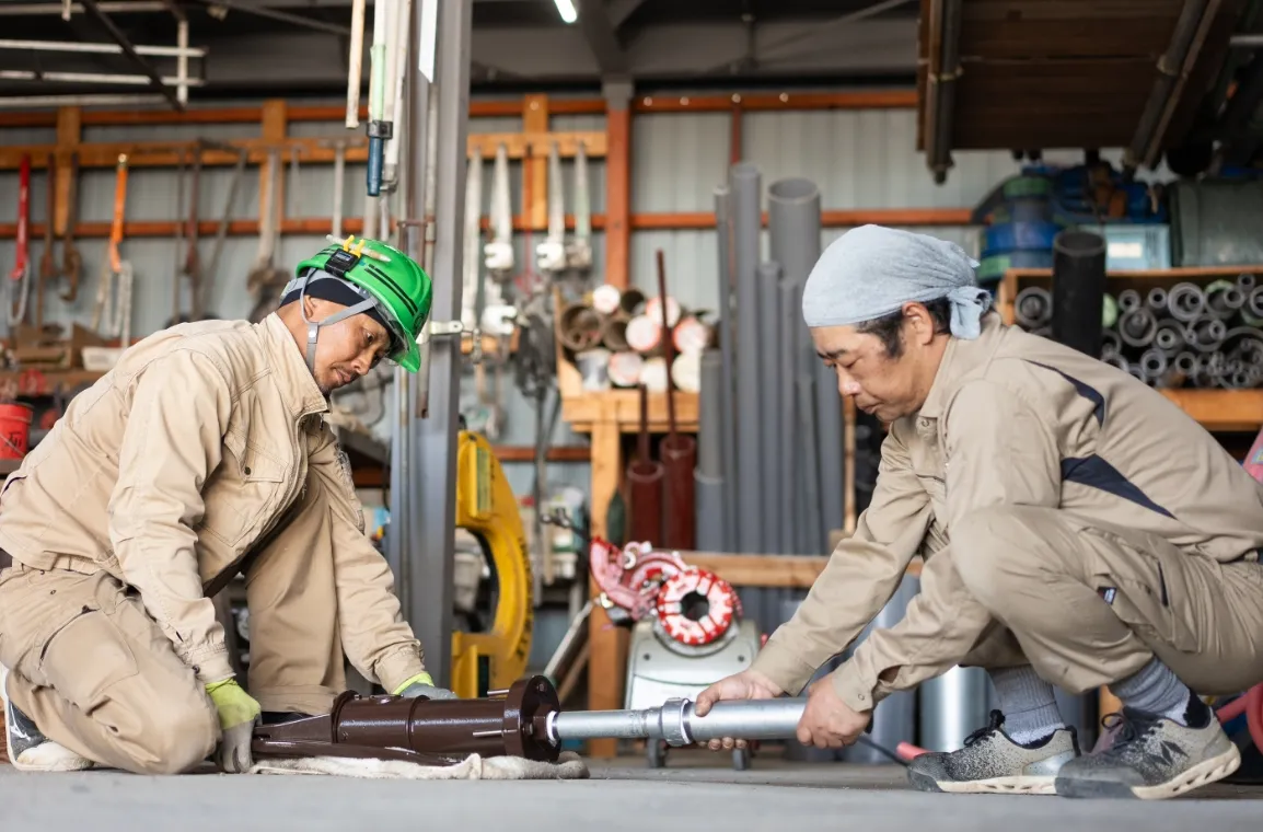 作業服を着た2人の男性が工場内で金属部品を組み立てている様子