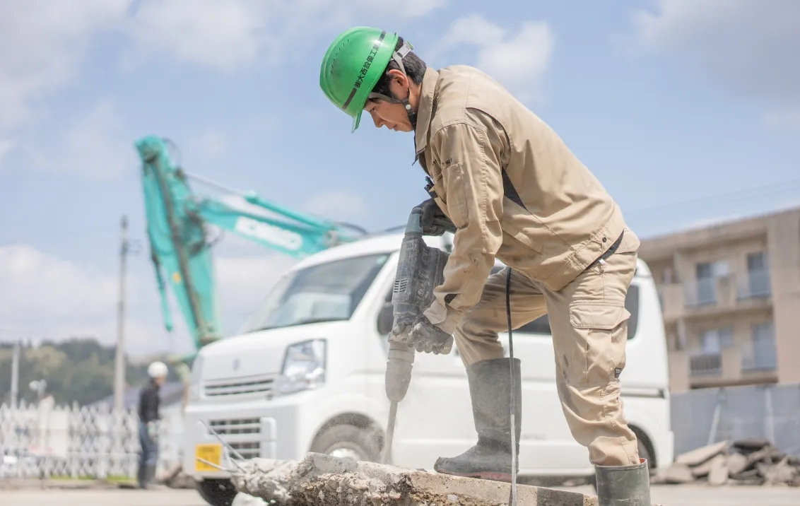 緑のヘルメットをかぶった作業員が、電動工具を使ってコンクリートを削っている