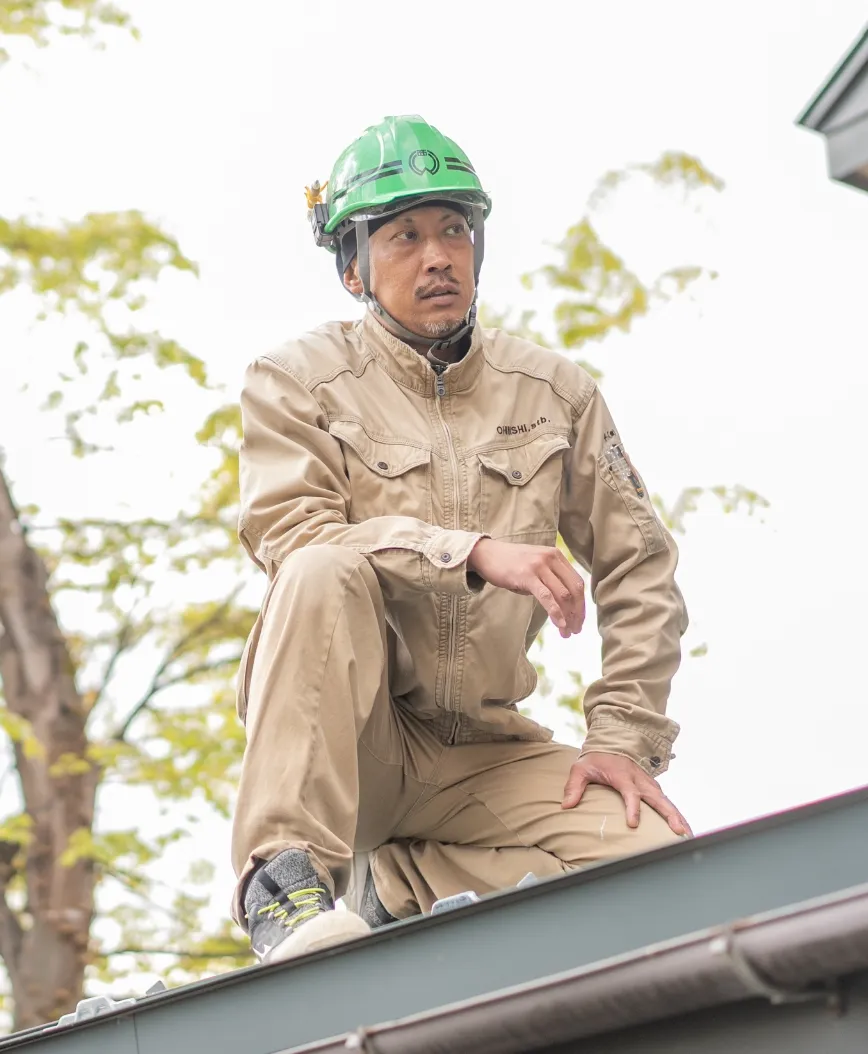 作業服とヘルメットを着用した男性が屋根の上で作業中にしゃがんでいる様子