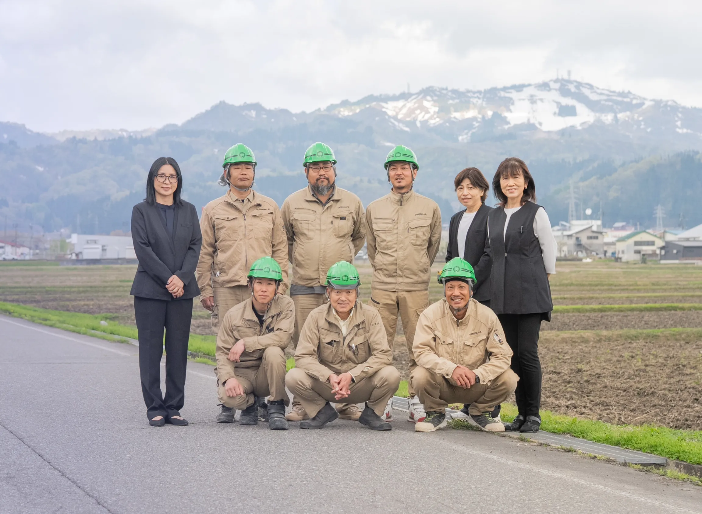 山あいの田畑を背景に笑顔で並ぶ社員たち