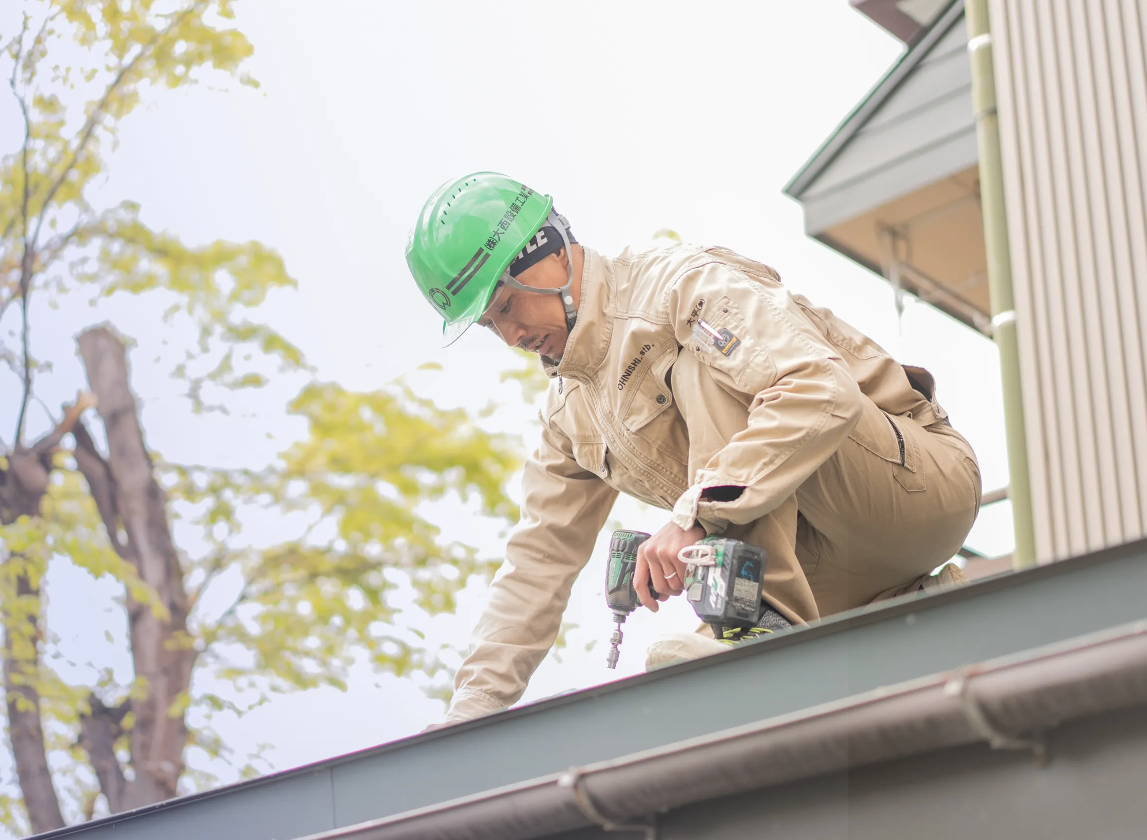 緑のヘルメットをかぶった作業員が、建物の屋根でドリルを使って作業中