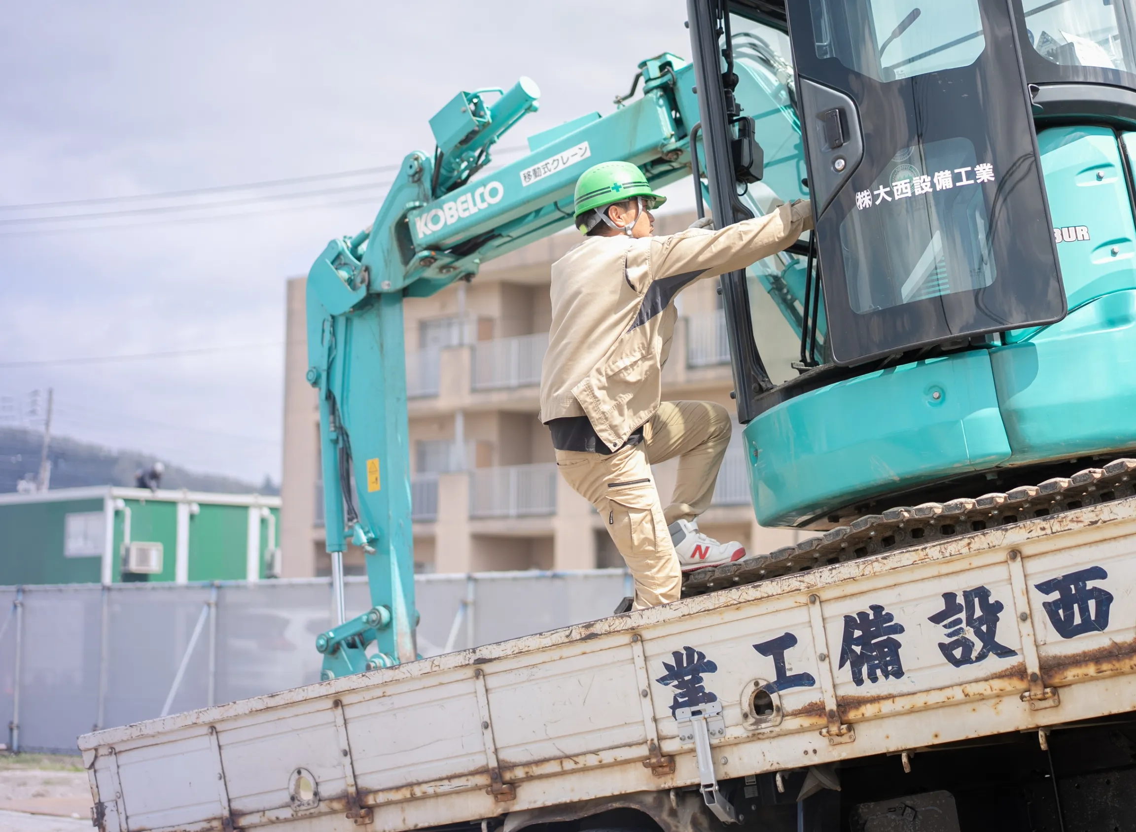 作業員がトラックの荷台に積まれた重機に乗り込もうとしている様子