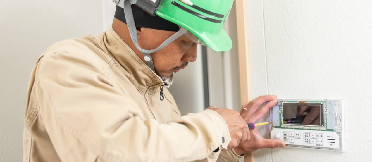 小型のドライバーを使用して、インターホンの外装パネルを慎重に操作している様子